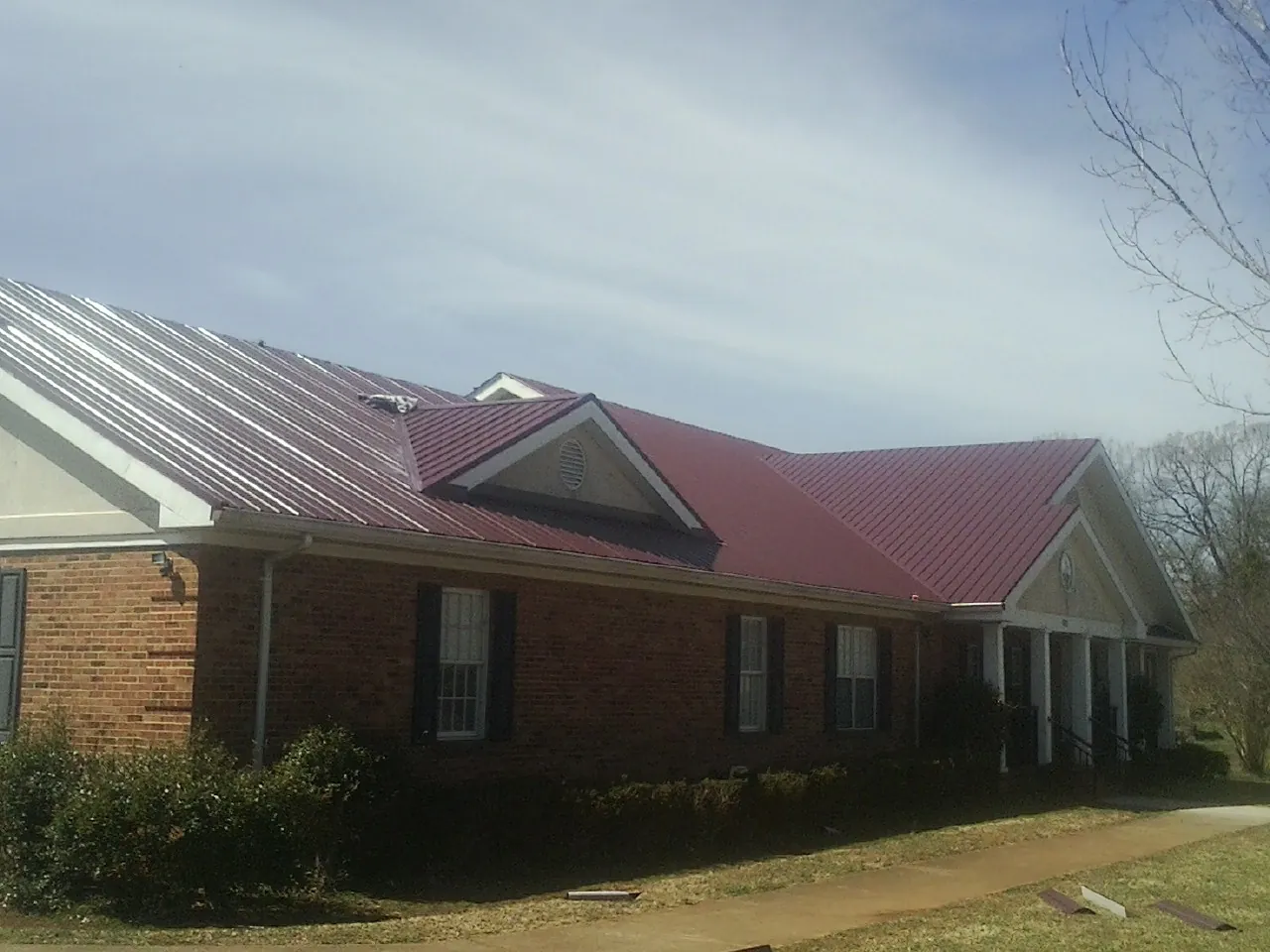 Red metal roof with gabled entries on a long brick building, from a Hail Damage Roof Repair job in Goldsboro
