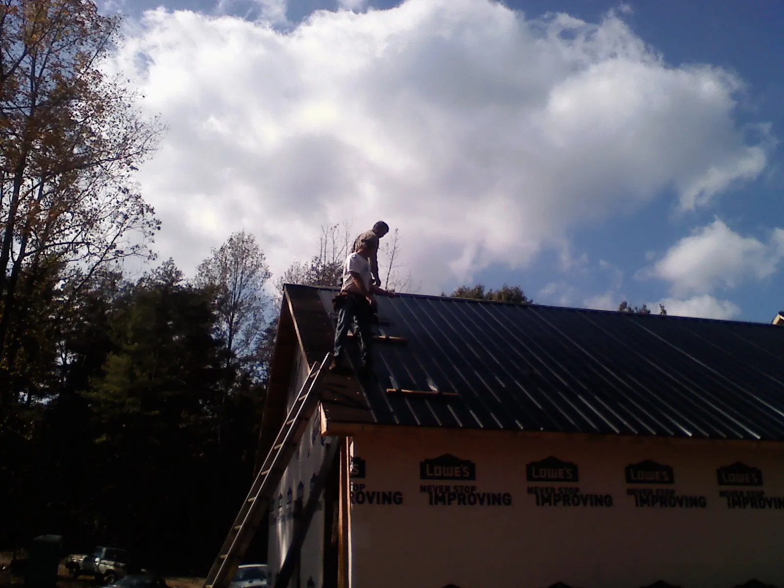 Roofer fastening dark metal panels high against a cloudy sky, from a Roof Inspection job in Goldsboro