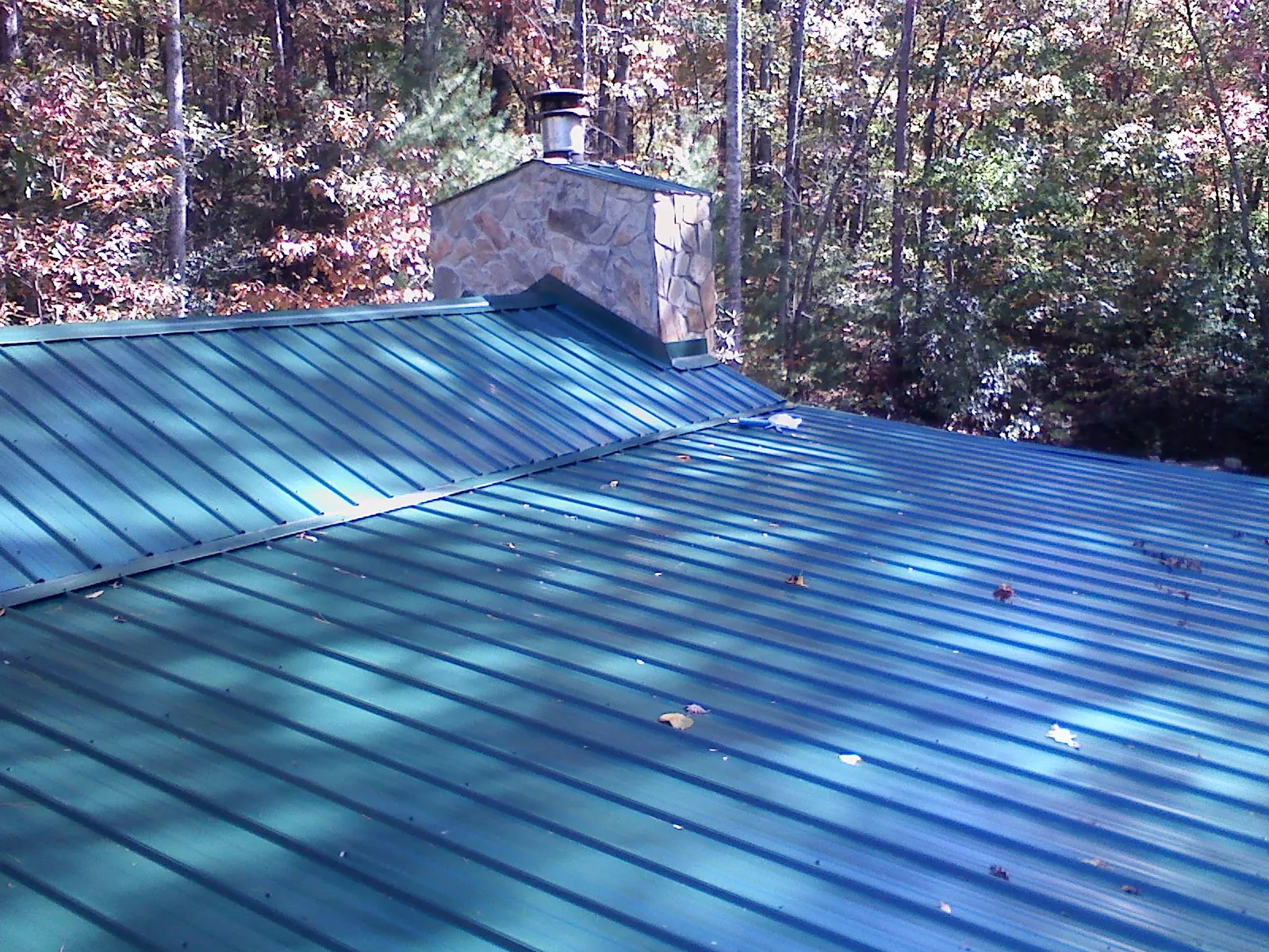 New green metal roof and stone chimney surrounded by autumn woods in Goldsboro